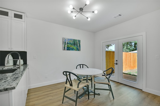 dining room featuring sink, french doors, a chandelier, and light wood-type flooring