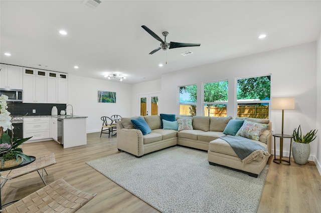 living room featuring ceiling fan, french doors, sink, and light wood-type flooring