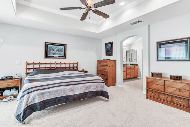 carpeted bedroom featuring ceiling fan, a raised ceiling, crown molding, and ensuite bath