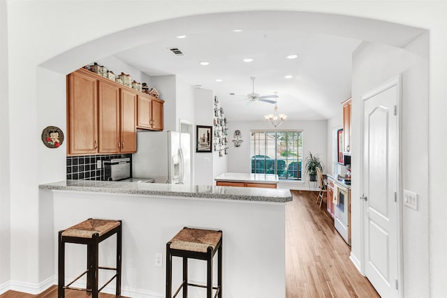 kitchen featuring kitchen peninsula, white appliances, a breakfast bar area, decorative backsplash, and light wood-type flooring