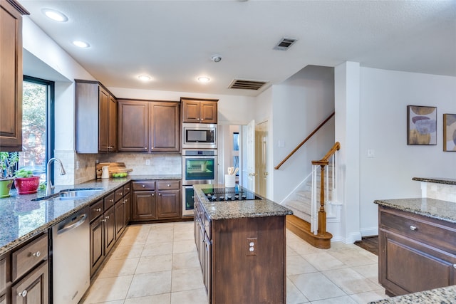 kitchen featuring decorative backsplash, appliances with stainless steel finishes, light stone counters, sink, and a kitchen island