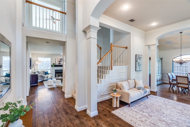 entryway with a high ceiling, crown molding, ornate columns, a notable chandelier, and dark hardwood / wood-style flooring