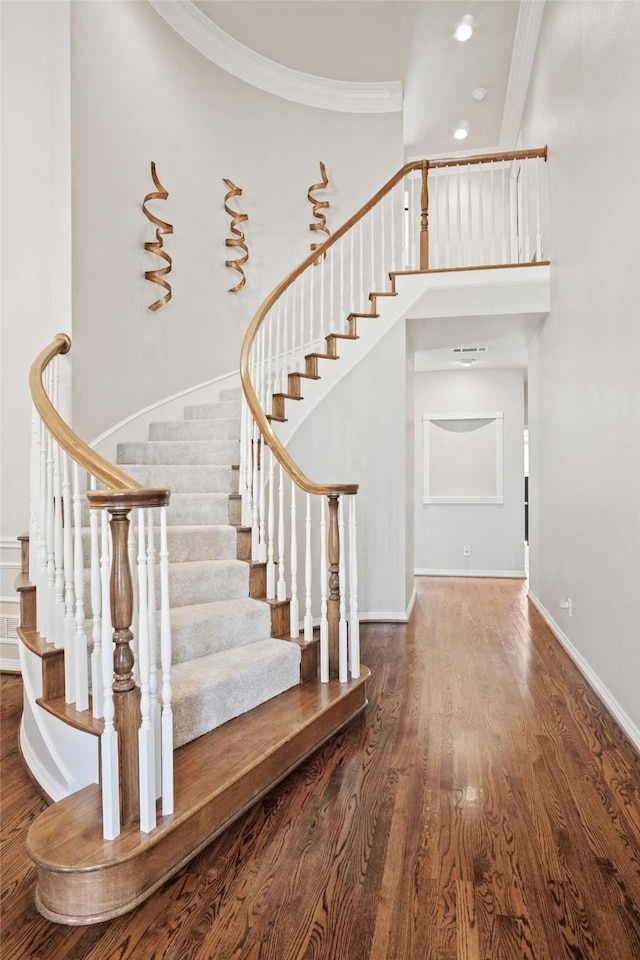 stairway with a high ceiling, crown molding, and hardwood / wood-style floors