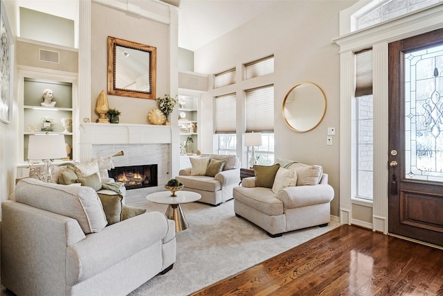 living room with dark hardwood / wood-style flooring, a towering ceiling, built in features, and a fireplace