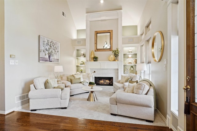 living room with hardwood / wood-style flooring, a towering ceiling, a high end fireplace, and built in features