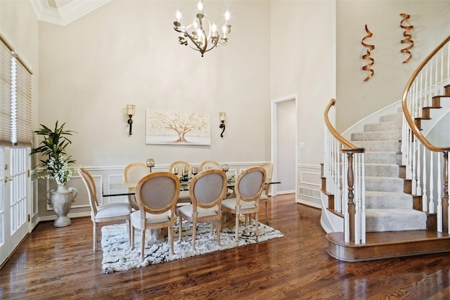 dining area with dark wood-type flooring, ornamental molding, an inviting chandelier, and a high ceiling