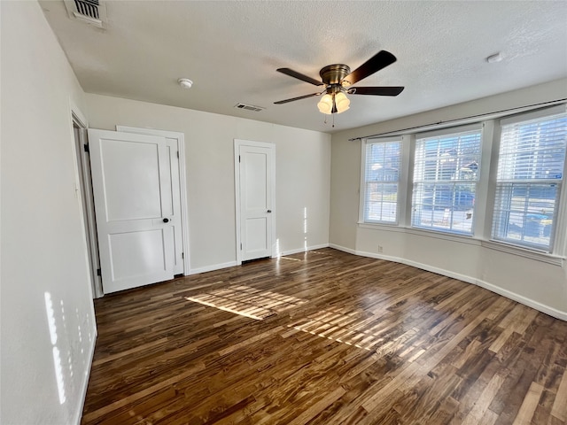 unfurnished bedroom featuring connected bathroom, a barn door, ceiling fan, and dark wood-type flooring