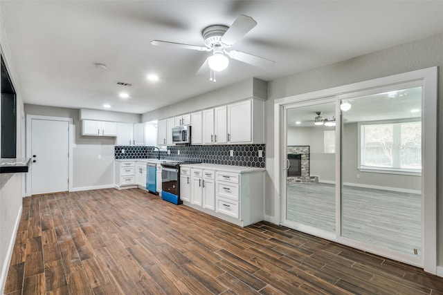 kitchen with dark hardwood / wood-style flooring, stainless steel appliances, ceiling fan, white cabinets, and a stone fireplace