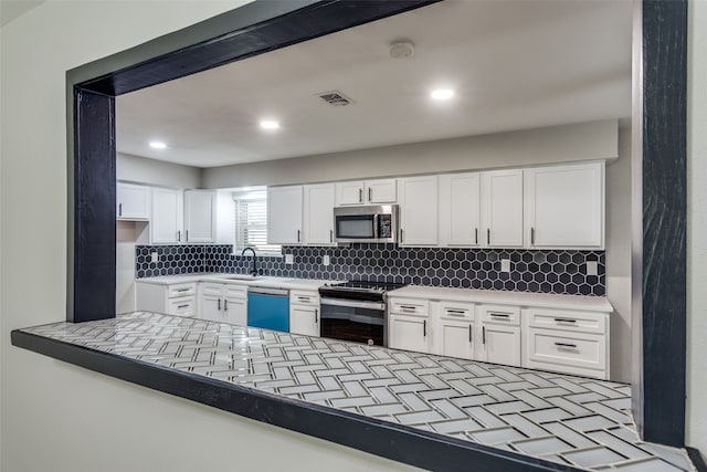 kitchen with kitchen peninsula, backsplash, stainless steel appliances, sink, and white cabinetry