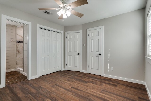 unfurnished bedroom with connected bathroom, ceiling fan, dark wood-type flooring, and two closets