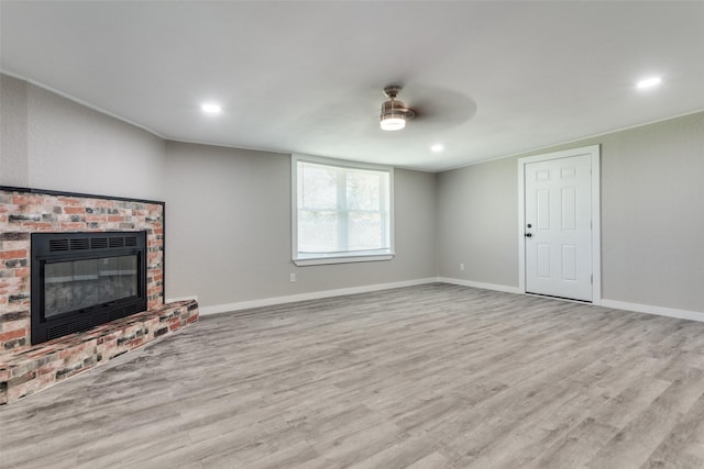 unfurnished living room featuring a brick fireplace, ceiling fan, and light wood-type flooring