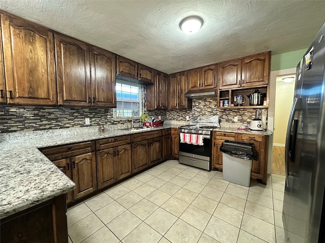 kitchen with appliances with stainless steel finishes, sink, decorative backsplash, dark brown cabinetry, and light stone counters