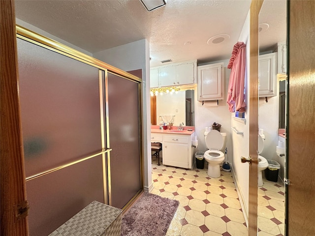 bathroom with a shower with door, vanity, a textured ceiling, and toilet