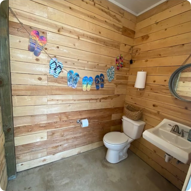 bathroom with concrete floors, sink, wood walls, and toilet