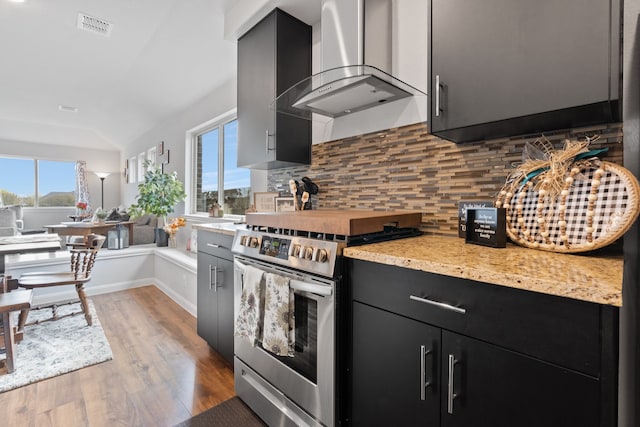 kitchen with lofted ceiling, wall chimney range hood, high end stainless steel range oven, tasteful backsplash, and light hardwood / wood-style floors