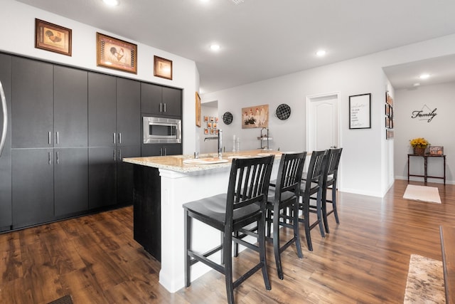 kitchen featuring stainless steel microwave, sink, dark hardwood / wood-style flooring, a kitchen island with sink, and a breakfast bar