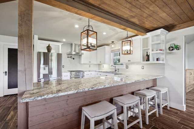 kitchen with white cabinets, stainless steel appliances, kitchen peninsula, and wall chimney range hood