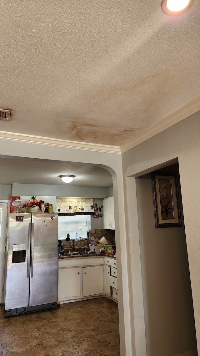 kitchen featuring white cabinets, sink, stainless steel refrigerator with ice dispenser, ornamental molding, and a textured ceiling