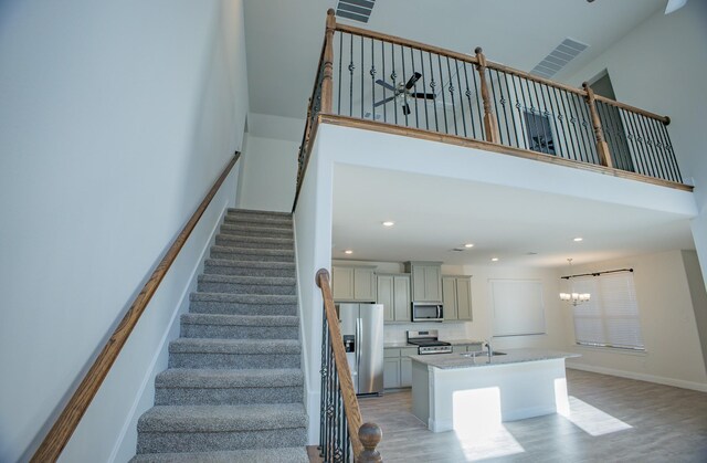 stairway with a notable chandelier, wood-type flooring, sink, and a high ceiling