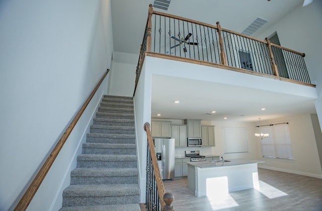 stairs featuring a notable chandelier, wood-type flooring, sink, and a high ceiling