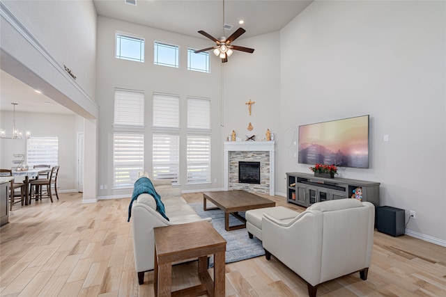 living room featuring ceiling fan with notable chandelier, a stone fireplace, a wealth of natural light, and light wood-type flooring