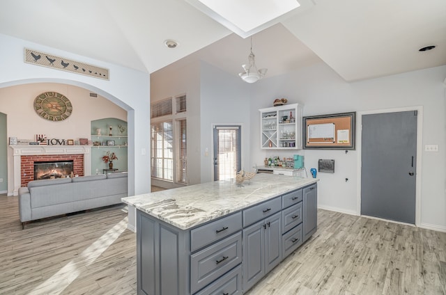 kitchen with light stone counters, light hardwood / wood-style flooring, a fireplace, a kitchen island, and hanging light fixtures