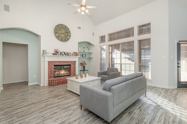 living room featuring ceiling fan, light wood-type flooring, a fireplace, and high vaulted ceiling