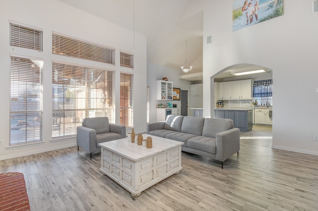 living room with sink, high vaulted ceiling, and light wood-type flooring