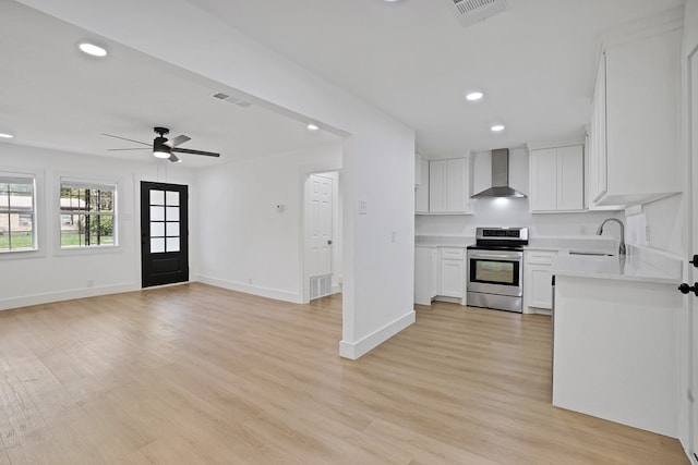 kitchen with sink, stainless steel stove, wall chimney exhaust hood, light wood-type flooring, and white cabinetry