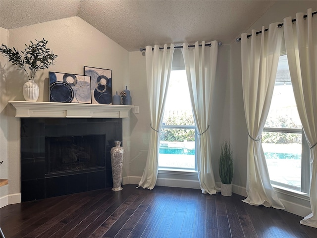 unfurnished living room with a textured ceiling, dark wood-type flooring, a tile fireplace, and vaulted ceiling