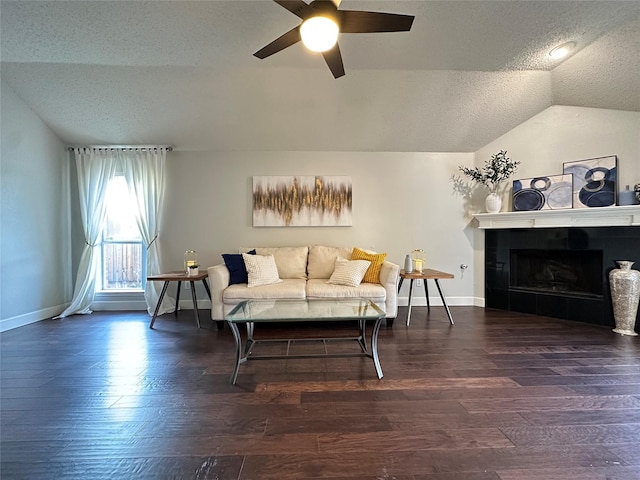 living room featuring a textured ceiling, vaulted ceiling, ceiling fan, dark hardwood / wood-style floors, and a tiled fireplace