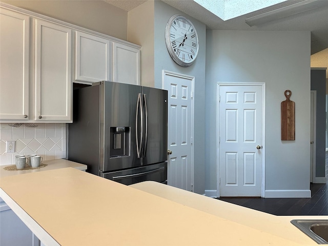 kitchen with a skylight, white cabinetry, dark hardwood / wood-style floors, stainless steel fridge, and decorative backsplash