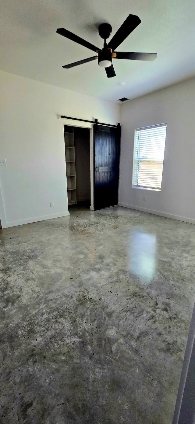 unfurnished bedroom featuring a barn door, concrete floors, and ceiling fan