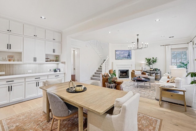 dining space with light wood-style floors, recessed lighting, a warm lit fireplace, and stairs