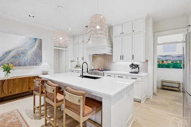 kitchen with a sink, white cabinets, light wood-type flooring, backsplash, and a center island with sink