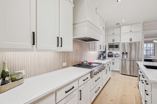 kitchen featuring white cabinets, light wood-style flooring, custom range hood, stainless steel appliances, and light countertops