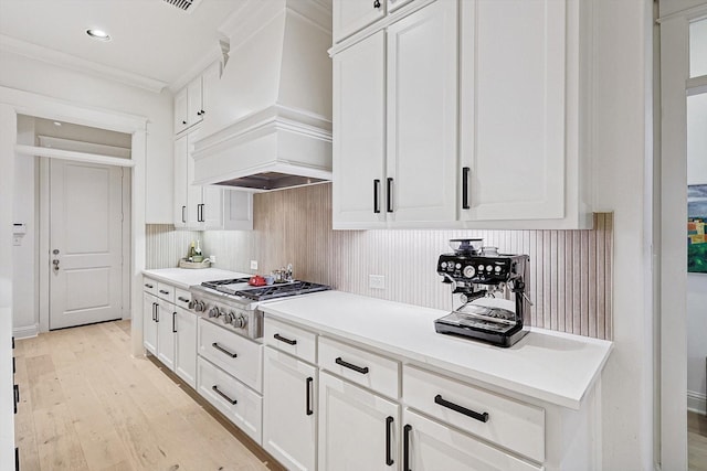 kitchen with crown molding, premium range hood, stainless steel gas stovetop, and white cabinetry