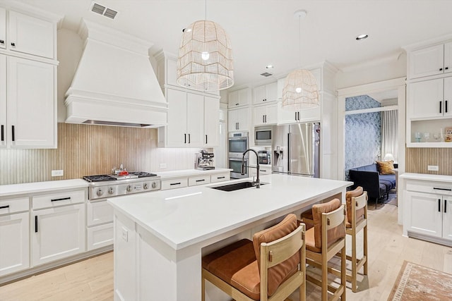 kitchen with visible vents, appliances with stainless steel finishes, light wood finished floors, a center island with sink, and custom range hood