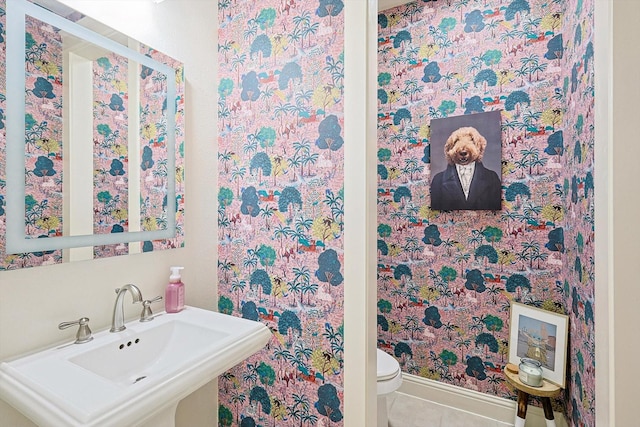 half bath featuring tile patterned flooring, a sink, toilet, and baseboards