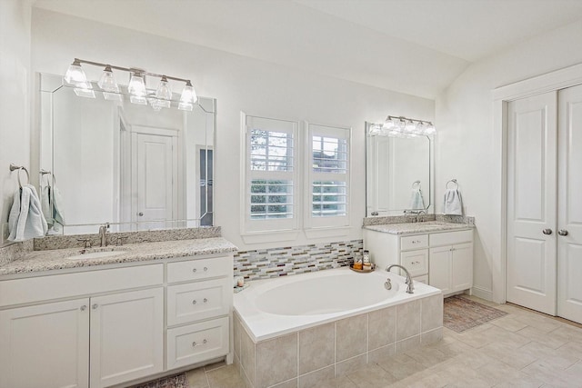 bathroom with lofted ceiling, two vanities, a sink, and a bath