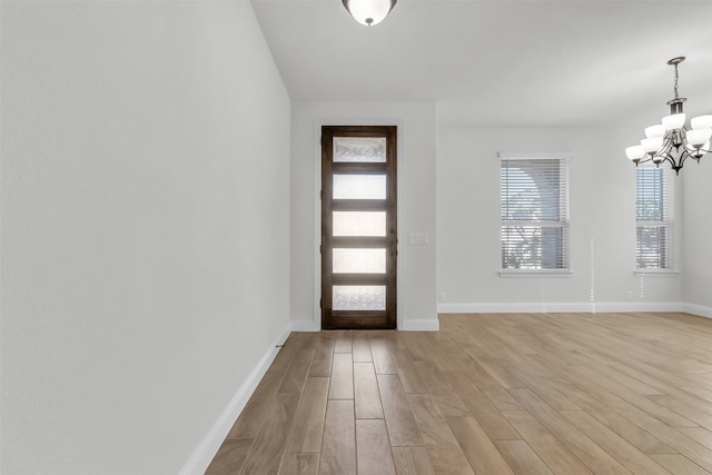 foyer entrance with plenty of natural light, light wood-type flooring, and a chandelier