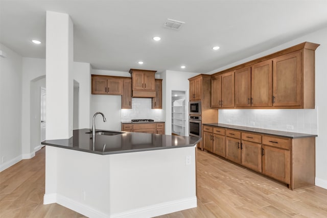 kitchen with sink, stainless steel appliances, tasteful backsplash, an island with sink, and light wood-type flooring