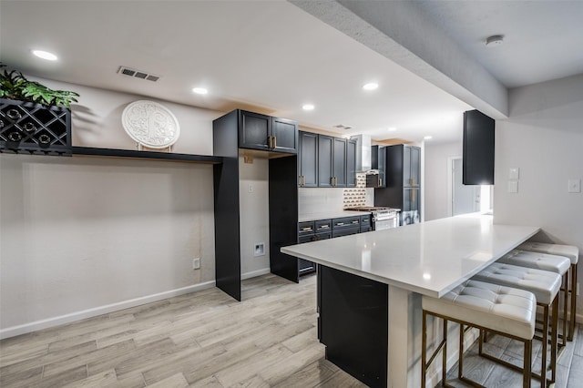 kitchen featuring a kitchen bar, decorative backsplash, kitchen peninsula, stainless steel gas range, and light hardwood / wood-style flooring