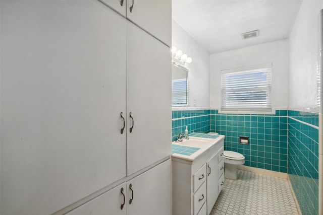 bathroom featuring tile patterned floors, vanity, toilet, and tile walls