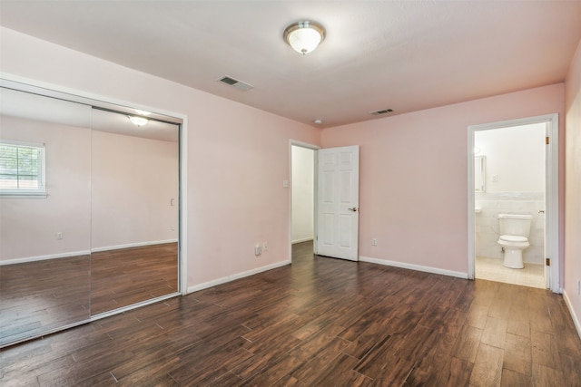 unfurnished bedroom featuring ensuite bath, a closet, dark wood-type flooring, and tile walls