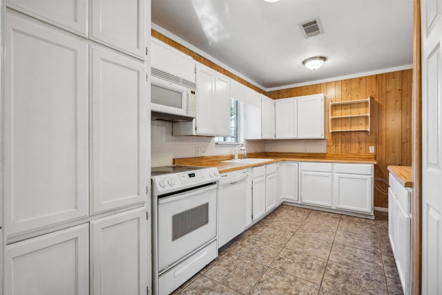 kitchen with wood walls, white appliances, white cabinets, sink, and tasteful backsplash