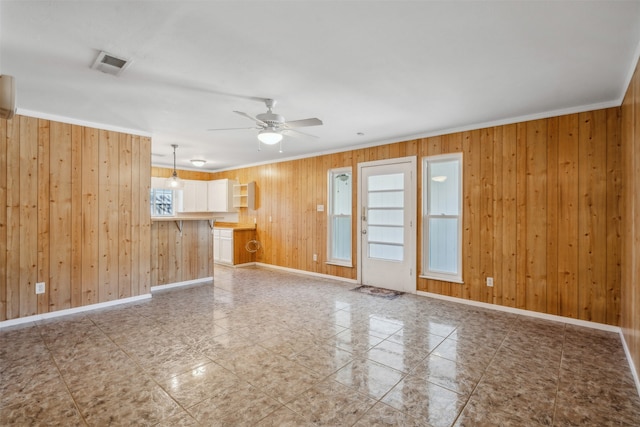 unfurnished living room featuring wood walls, crown molding, and ceiling fan