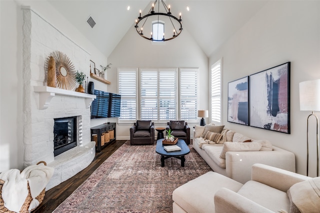 living room featuring a notable chandelier, a healthy amount of sunlight, dark hardwood / wood-style flooring, and a stone fireplace