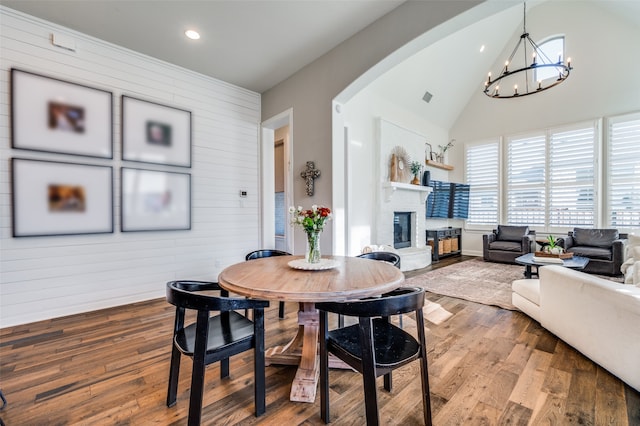 dining area featuring lofted ceiling, wood-type flooring, wooden walls, and an inviting chandelier