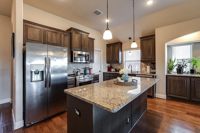 kitchen with backsplash, stainless steel appliances, decorative light fixtures, dark hardwood / wood-style floors, and a kitchen island